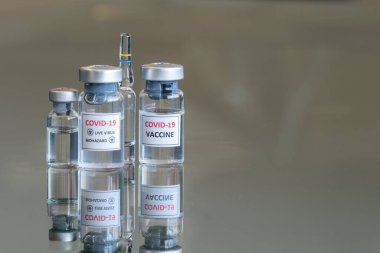 COVID-19 Coronavirus olarak etiketlenmiş tıbbi şişelerin yakından görüntüsü. Virüs biyolojik tehlike aşısı ilacı askıya alındı ve arkada ampul var. 033