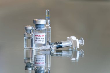 COVID 19 Coronavirus olarak etiketlenmiş tıbbi şişelerin yakından görüntüsü. Virüs biyolojik tehlike aşısı ilacı. Bir ampul ve dolu bir şırınga ile askıya alındı.