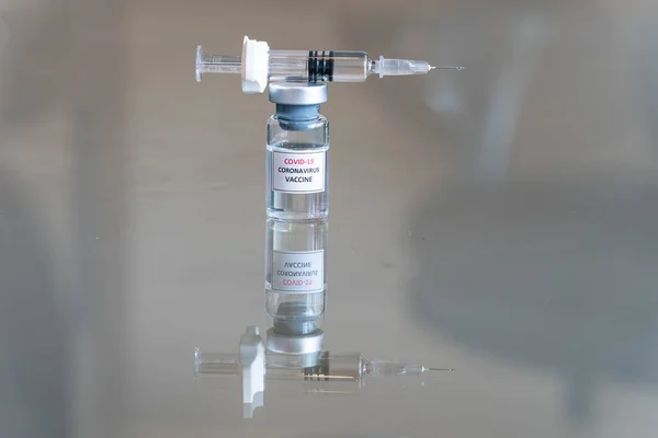 COVID-19 Coronavirus aşısı olarak etiketlenmiş bir tıbbi şişenin yakından görüntüsü. İlaç dozunu askıya alma çözeltisi. Üzerinde dolu bir şırınga ve keskin bir iğne var.