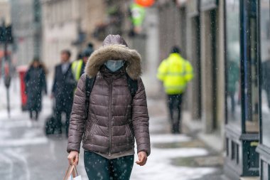 Londra, İngiltere - Şubat 2021: 016 'da soğuk bir kış günü Holborn London' da kar yağarken maske takan kürklü genç bir kadın
