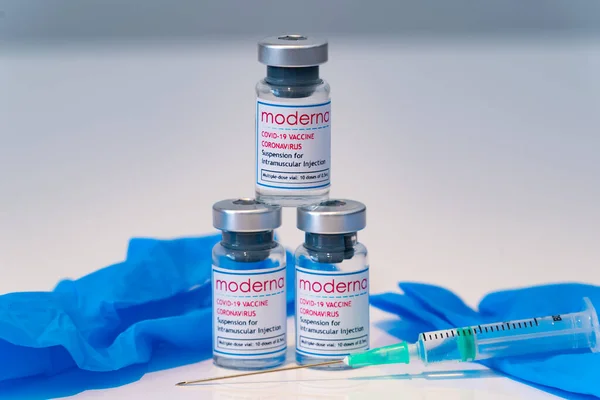 LONDON, ENGLAND - 28 Şubat 2021: Moderna COVID Coronavirus COVID 19 aşısı içeren üç cam şişe şırınga ve mavi lateks cerrahi eldiven - 028