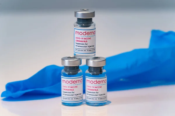LONDON, ENGLAND - 28 Şubat 2021: Arka planda mavi lateks cerrahi eldivenli Moderna COVID Coronavirus COVID-19 aşısı içeren üç cam şişe yığını - 024