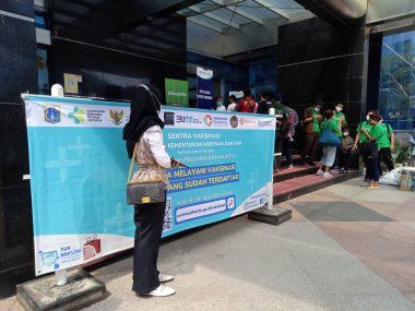 Editör Fotoğrafı, Endonezya, Güney Cakarta, 08 Juli 2021, Smesco Binası, Banner Covid-19 aşısı yakınında duran insanlar