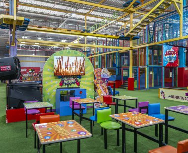 Renkli oyun yapıları, masalar, sandalyeler ve eğlence alanlarının yer aldığı belgesel kapalı çocuk aktiviteleri merkezi.