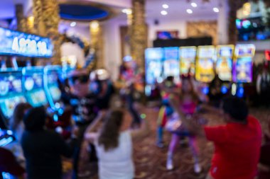 Soyut bulanık kumarhane sahnesi renkli ışıklar, kumar makineleri ve insanların siluetlerini gösteriyor. Canlı Bokeh etkisi, eğlence ve gece hayatı temaları için ideal enerjik ve atmosferik bir arka plan yaratır..