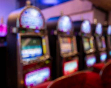 Mor, pembe ve mavi ışıklarla parlayan klasik slot makinelerinin soyut bulanık satırı. Yumuşak bokeh eğlenceli ve dijital arka planlar için ideal renkli, sıcak ve canlı bir kumarhane atmosferi yaratır..