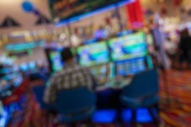 Parlak kollu makinelerde oturan bir adamla bulanık kumarhane ortamı. Renkli ışıklandırma ve soyut yumuşak odak etkisi kumar ve gece hayatı temaları için ideal canlı bir eğlence ortamı yaratıyor..