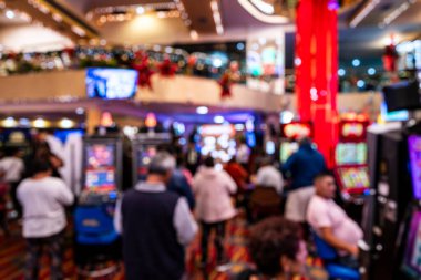 Kumarhanenin içi insanlarla ve kumar makineleriyle bulanık. Parlak ışıklar ve şenlikli dekorasyonlar gösteriyorlar. Hareketli ve enerjik bir ortam yaratıyorlar..