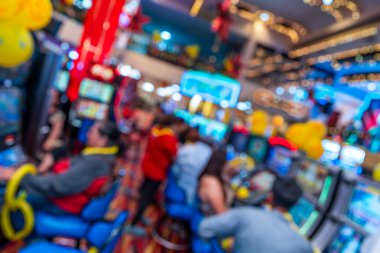 Bulanık oyuncuların, kumar makinelerinin, parlak dijital ekranların, balonların ve şenlikli dekorasyonların olduğu yumuşak odaklı kumarhane ortamı. Görüntü, hareketli eğlence, hareket, renk ve modern oyun atmosferini aktarır..