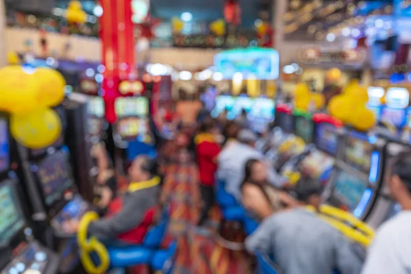 Bulanık oyuncuların, kumar makinelerinin, parlak dijital ekranların, balonların ve şenlikli dekorasyonların olduğu yumuşak odaklı kumarhane ortamı. Görüntü, hareketli eğlence, hareket, renk ve modern oyun atmosferini aktarır..