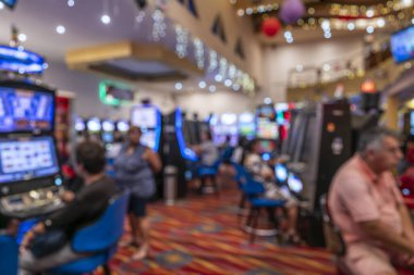 Işık saçan bir kumarhanede kumar oynayan insanları bulanık görmek, renkli ekranlar, desenli halı ve yumuşak odaklı ışıklandırma ve hareketle güçlendirilmiş canlı ortam..