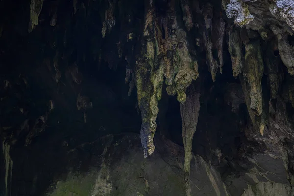 Sarkıtlar ve engebeli mineral kaya oluşumları doğal bir mağara girişinden sarkan jeolojik dokuları, derin gölgeleri, erozyon detaylarını ve dramatik bir yeraltı ortamındaki toprak tonlarını gösteriyor..