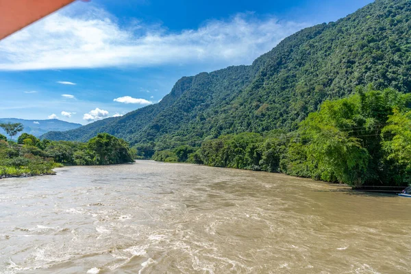 Ro Monzn, Peru Tingo Mara 'da yemyeşil dağların yanında akıyor. Parlak gökyüzü, yoğun bitki örtüsü ve canlı tropikal manzara seyahat, doğa ve açık hava temaları için ideal doğal bir manzara yaratır..