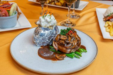 Mantar soslu fileminyon, kuşkonmaz ve folyoyla sarılmış kremalı patates, restoran ortamında seramik tabakta, gurme aromalı, zarif bir sunum, kaliteli bir yemek tarzı.