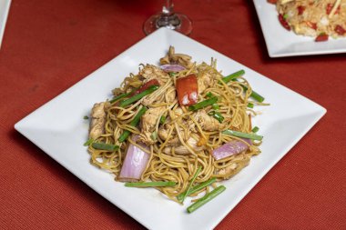 Peru tavuğu, kırmızı masa örtüsü üzerinde beyaz kare bir tabakta sebzeli kızarmış erişte, restoran markası, menüler ve yemek promosyonu için ideal..