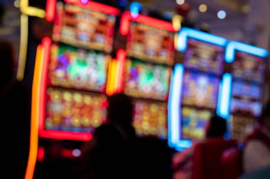 Kumar makineleri, neon ışıkları ve siluetleri olan bulanık bir kumarhane. Renkli ışıltı, gece hayatı, eğlence, eğlence, eğlence, şans ve risk ile bağlantılı soyut bir kumar ortamı yaratır.