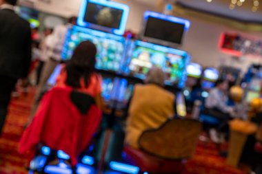 Kumarhane salonundaki kumar makinelerinde oynayan bulanık insanlar. Renkli ekranlar, parlak ışıklar ve dijital ekranlar kumar eğlence ve eğlence odaklı aktif bir atmosfer yaratıyor.