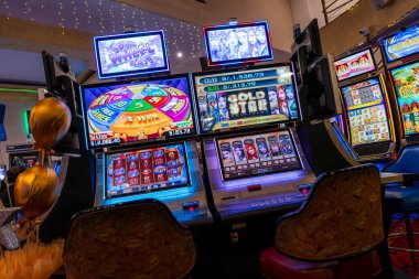 Modern bir kumarhane kumarhanesinde aydınlatılmış kumar makineleri. Dijital ekranlar parlak ışıklar ve renkli ekranlar kumar eğlence teknolojisi ve gece hayatına odaklanmış bir eğlence ortamı yaratıyor.