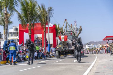 Askerlerin eşlik ettiği zırhlı bir askeri araç ve taktik polis ekipleri bir şehir caddesinde geçit töreni sırasında ilerliyorlar. İzleyiciler, Peru 'daki ulusal savunma, kamu güvenliği ve kurumsal varlığı vurguluyor.
