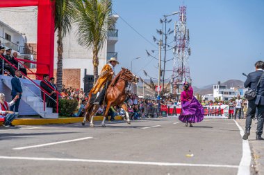 Marinera dansçıları, bir at binicisinin ve renkli kostümlerin yer aldığı bir sivil geçit töreninde geleneksel Peru dansı yapıyorlar. Seyirciler, Peru 'daki folklor, kültür mirası ve ulusal gururu ön plana çıkararak sokaktan izliyor.