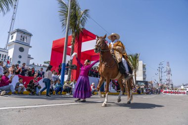 Marinera dansçıları, bir at binicisinin ve renkli kostümlerin yer aldığı bir sivil geçit töreninde geleneksel Peru dansı yapıyorlar. Seyirciler, Peru 'daki folklor, kültür mirası ve ulusal gururu ön plana çıkararak sokaktan izliyor.