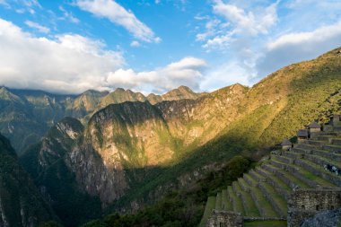 Machu Picchu 'dan Panoramik And Vadisi' ne dağ eteklerinde İnka terasları, dramatik uçurumlar, yeşil orman ve güneş ışığı. Antik mimari ve manzara Peru 'daki kültür mirası, arkeoloji, tarih ve seyahat turizm beldesini temsil etmektedir..