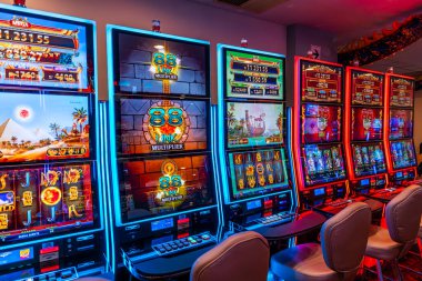 LED ekranlar, renkli grafikler ve aydınlatılmış çerçeveler içeren bir dizi modern kumarhane kumar makinesi. Oturma ve ışıklandırma, eğlence ve kumar temaları için mükemmel bir oyun ortamı yaratıyor..