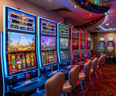 LED ekranlar, renkli grafikler ve aydınlatılmış çerçeveler içeren bir dizi modern kumarhane kumar makinesi. Oturma ve ışıklandırma, eğlence ve kumar temaları için mükemmel bir oyun ortamı yaratıyor..