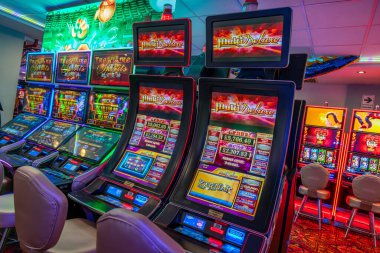 LED ekranlar, renkli grafikler ve aydınlatılmış çerçeveler içeren bir dizi modern kumarhane kumar makinesi. Oturma ve ışıklandırma, eğlence ve kumar temaları için mükemmel bir oyun ortamı yaratıyor..