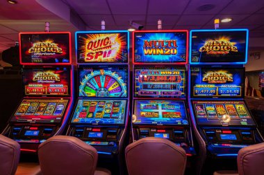 LED ekranlar, renkli grafikler ve aydınlatılmış çerçeveler içeren bir dizi modern kumarhane kumar makinesi. Oturma ve ışıklandırma, eğlence ve kumar temaları için mükemmel bir oyun ortamı yaratıyor..