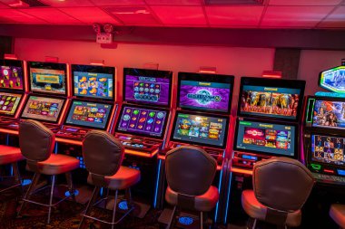 LED ekranlar, renkli grafikler ve aydınlatılmış çerçeveler içeren bir dizi modern kumarhane kumar makinesi. Oturma ve ışıklandırma, eğlence ve kumar temaları için mükemmel bir oyun ortamı yaratıyor..