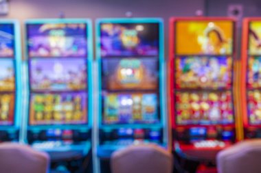 Renkli kollu kumar makineleri ve neon ışıkları olan modern bir kumarhane. Bulanık arka plan kumar, eğlence, oyun ve eğlence ile ilgili konular için uygun dinamik bir ortam yaratıyor..