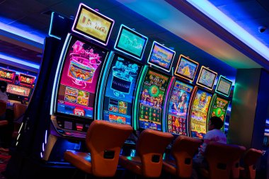 Kumarhanenin içinde renkli ekranları ve parlak neon ışıkları olan bir dizi ışıklı kumar makinesi. Sahnede yastıklı koltuklar, desenli halı ve kumar ve eğlence temaları için ideal canlı elektronik gösteriler yer alıyor..