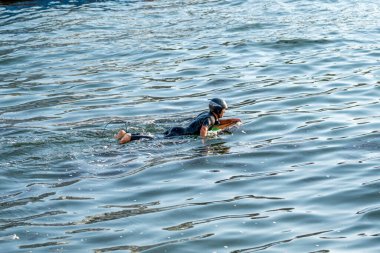 Açık deniz sahnesinde dalış kıyafeti ve kask giyerken sörf yapan biri görülüyor. Su sporları, deniz eğlencesi, sahil macerası, seyahat yaşam tarzı ve açık hava fitness kavramları için ideal..