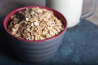 Koyu mavi arka planda sütlü kuru yulaf ezmesi. Seramik kasede sağlıklı mısır gevreği ve bir bardak yakın plan süt..