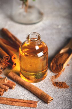 Temel tarçın yağı küçük bir şişede, tarçın ve tarçın çubukları taş zeminde.
