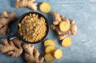 Taze zencefil kökü ve zemin zencefil baharatı mavi arka planda siyah kasede.