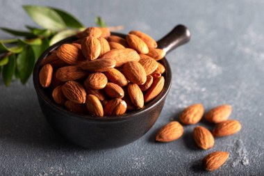 Taş zemin üzerinde siyah seramik kâse içinde çiğ badem yığını.