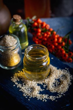 Cam ve tohumlu susam yağı. Cam şişede taze susam yağı ve mavi arka planda tohumlar..