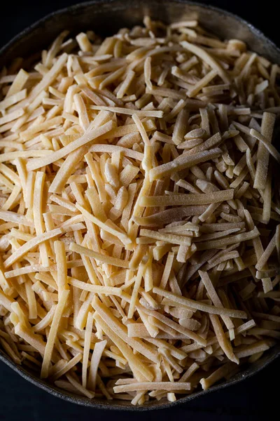 Koyu arkaplanda bir kase geleneksel Türk eriştesi (ham). Türk usulü el yapımı ahşap zemin üzerinde eriste (eriste).