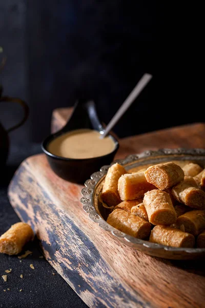 Geleneksel tahinili gevrek rulo ve tahin kabı ahşap arka planda. Tahini veya Tahini Çıtır ile Kuru Baklava.