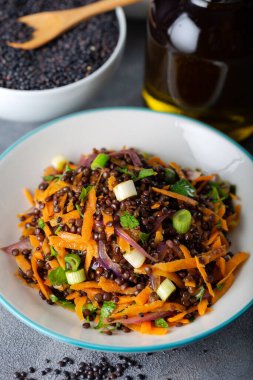 Havuçlu siyah mercimek salatası, soğan ve bir kase siyah mercimek ve gri arka planda maydanoz.