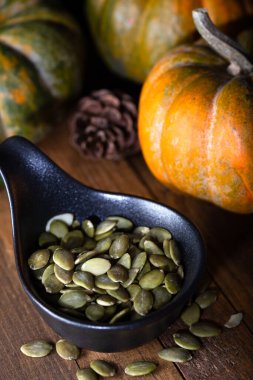 Ahşap zemin üzerinde siyah bir kasede kabak çekirdeği ve kabak kabukları. Yakın plan..