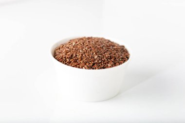 Beyaz arka planda beyaz kasede keten tohumları.