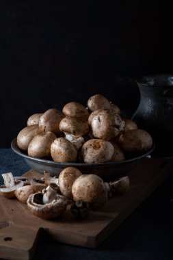 Taze şampiyon (düğme) mantarlar kasede, tahtanın üzerinde, arka planın önünde..