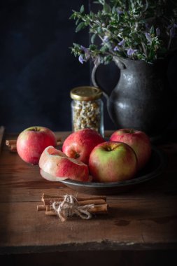 Doğal ahşap zemin üzerinde tarçın çubukları olan taze elmalar. Masanın üzerinde soyulmuş elma olan eski bir tabak..