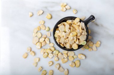 Kabuksuz, beyaz mermer üzerinde siyah bardakta küçük, kuru fasulye. Fava fasulyesi.