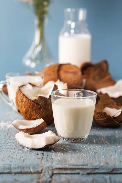Cracked coconut and glass of coconut milk on natural wooden background. Fresh coconut with milk.