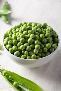 Ahşap zemin üzerinde taze bezelyeler olan bir kase. Beyaz kasedeki yeşil bezelyeler.