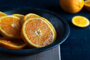 Taze portakal dilimlerinin yakın plan çekimi, tahtadan bir yüzey üzerinde koyu bir seramik kasede düzenlenmiştir..